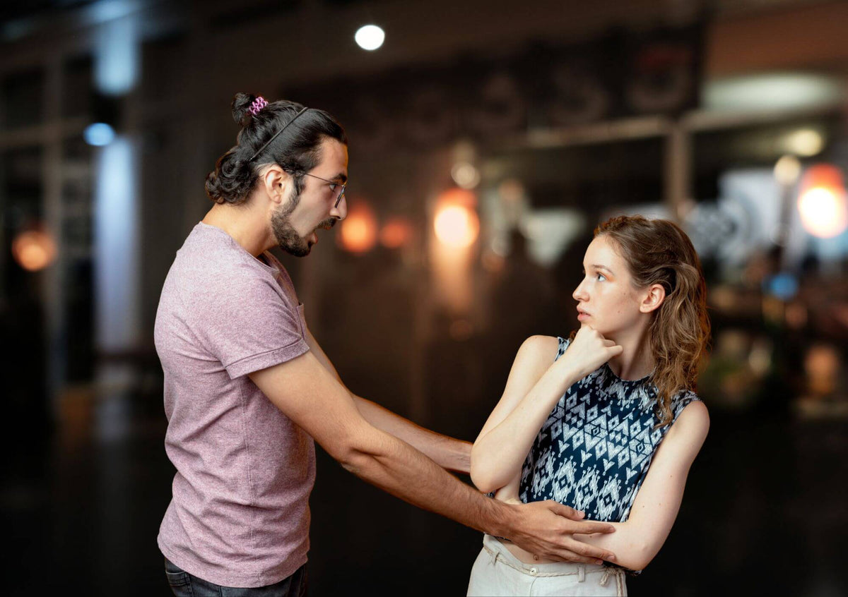 A woman visibly uncomfortable by an unknown male grabbing her to try to talk to her in a dark bar or pub. 
