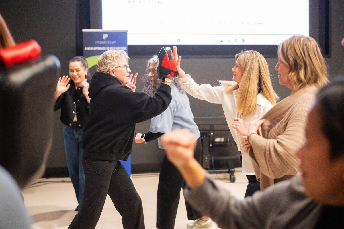 Employees practicing hands-on self-defense strikes using focus mitts during corporate training