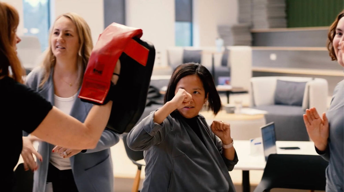 Person wearing boxing gloves in a casual office setting with colleagues observing.