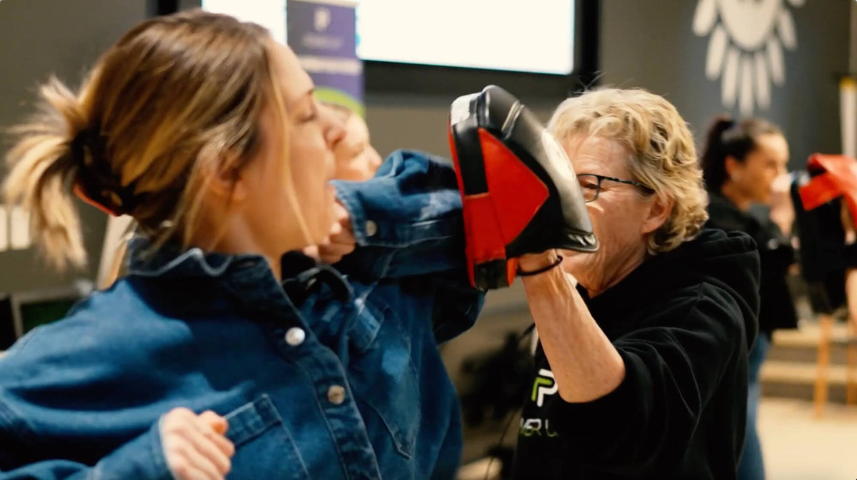 Two women practicing self-defense techniques in a classroom setting.