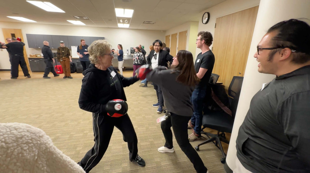 Lisa Davis holding a focus pad as a laughing college student strikes it during a campus self-defense class