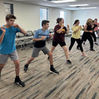 A group of people engaging in a self-defense class, standing and practicing defensive maneuvers.