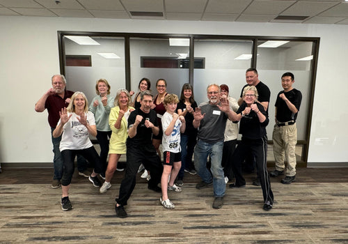 A group of people smiling and posing a self-defense move after a class